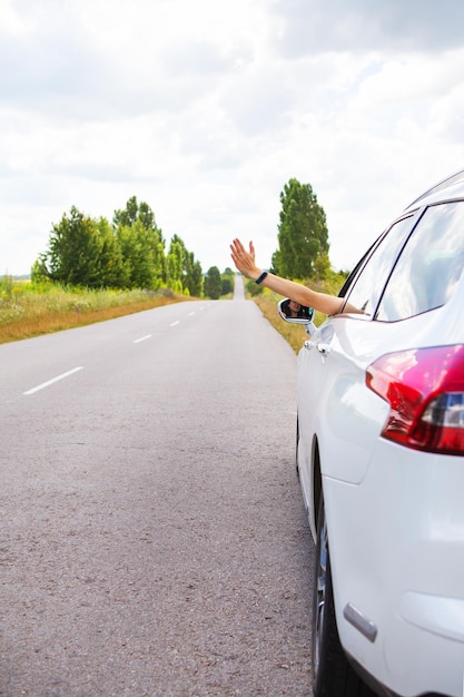 A young girl driving a car pulling her hand out of the window stops the car for help