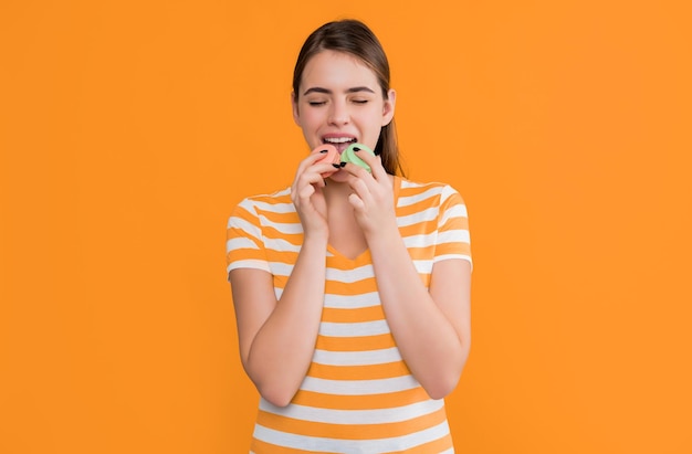 Photo young girl eating macaron on yellow background