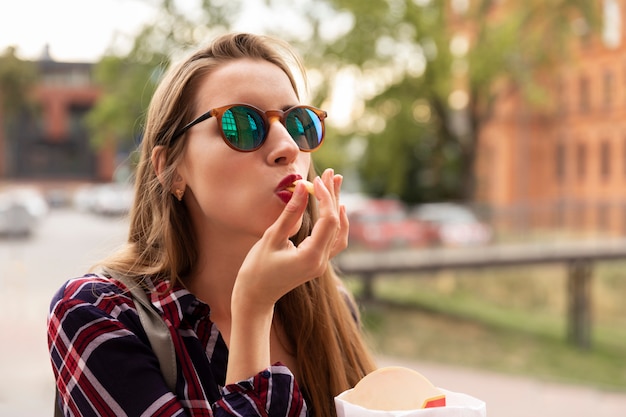 A young girl eats her french fries right on the street. She is very hungry, brutal appetite awoke in her.