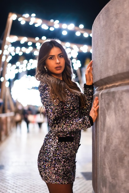 Young girl in a fashionable dress with sequins in the city christmas lights