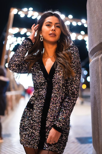 Young girl in a fashionable dress with sequins in the city christmas lights