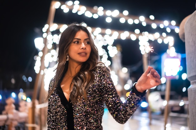 Young girl in a fashionable dress with sequins in the city christmas lights