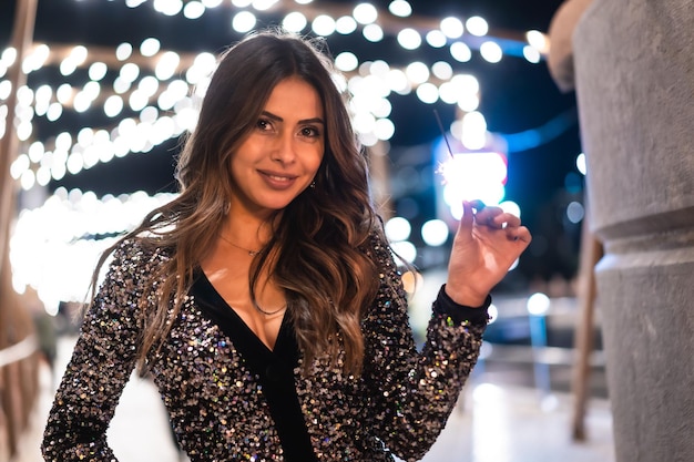 Young girl in a fashionable dress with sequins in the city christmas lights