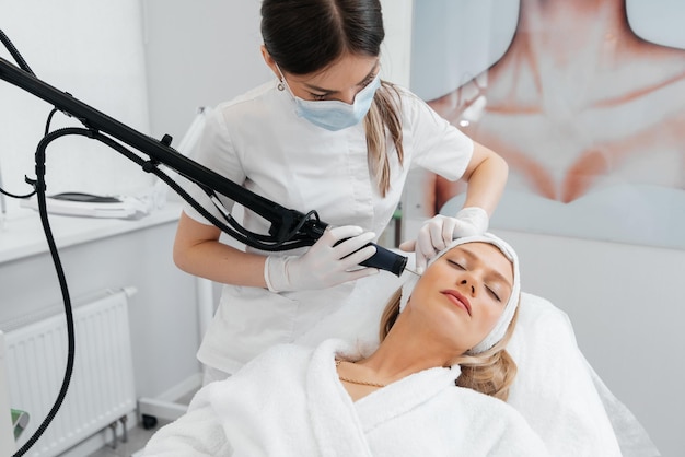 A young girl gets a charcoal peeling for the skin of the face in a beauty salon Laser pulses cleanse the skin Hardware cosmetology The process of photothermolysis warming the skin