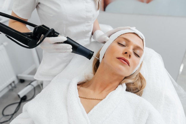 A young girl gets a charcoal peeling for the skin of the face in a beauty salon Laser pulses cleanse the skin Hardware cosmetology The process of photothermolysis warming the skin