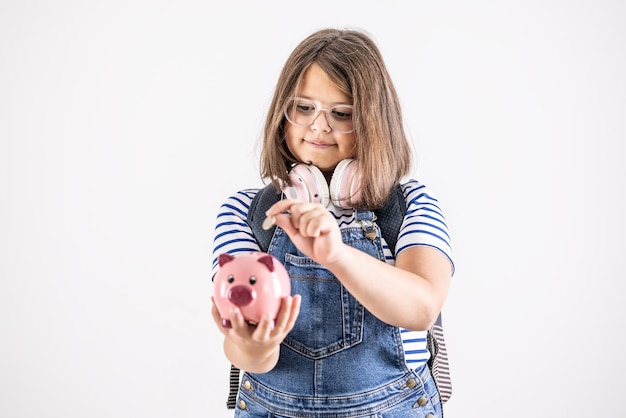 Young girl in glasses puts a coin into a piggybank