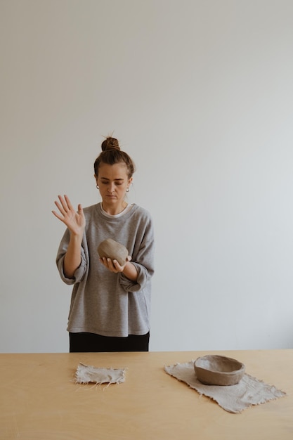 A young girl in a grey long sleeve makes a vase of clay with her own hands in a sculpture workshop