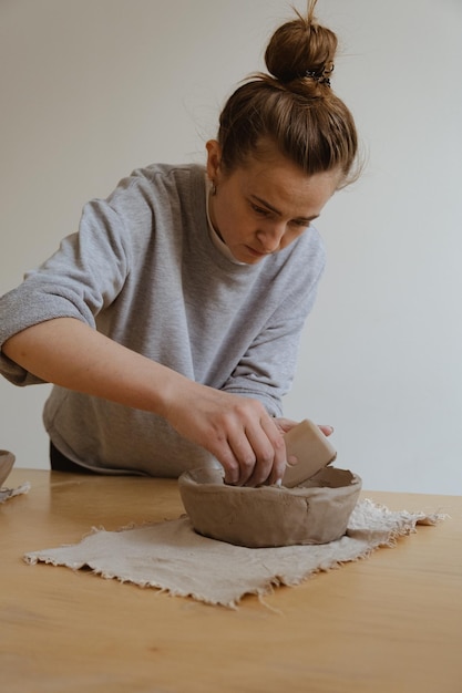 A young girl in a grey long sleeve makes a vase of clay with her own hands in a sculpture workshop