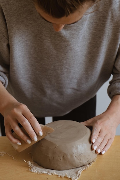 A young girl in a grey long sleeve makes a vase of clay with her own hands in a sculpture workshop