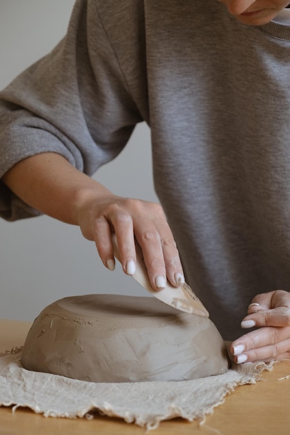 A young girl in a grey long sleeve makes a vase of clay with her own hands in a sculpture workshop