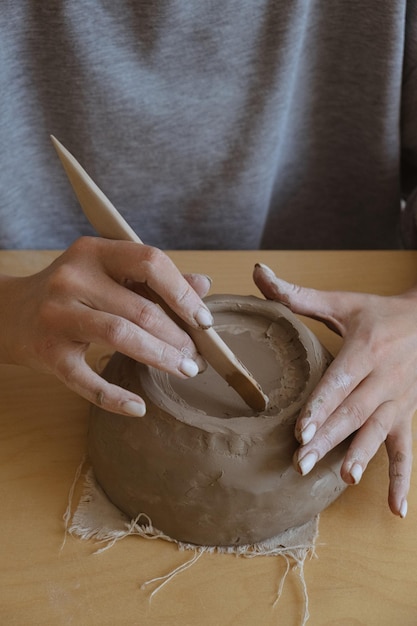 A young girl in a grey long sleeve makes a vase of clay with her own hands in a sculpture workshop