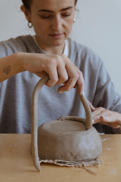 A young girl in a grey long sleeve makes a vase of clay with her own hands in a sculpture workshop