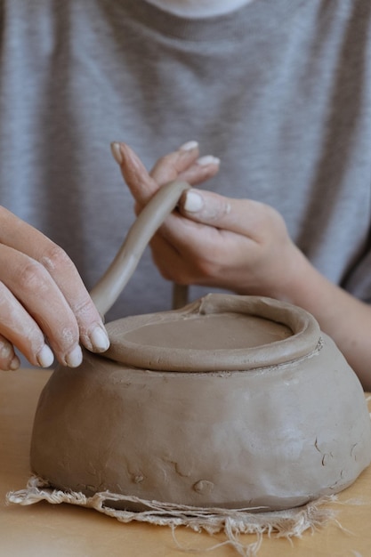 A young girl in a grey long sleeve makes a vase of clay with her own hands in a sculpture workshop