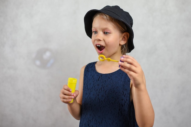 Young girl in a hat and dress blows bubbles