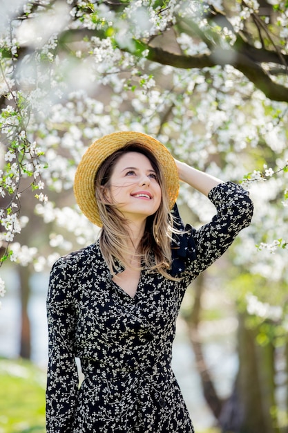 Young girl in a hat stay near a flowering tree in the park. Spring season