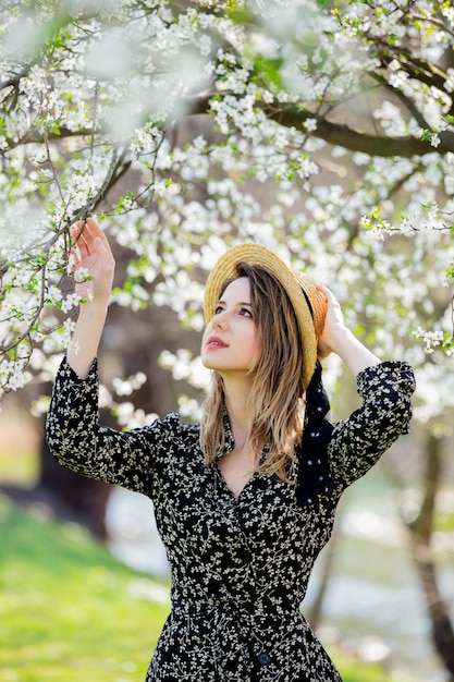 Young girl in a hat stay near a flowering tree 