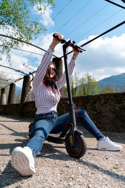 Young girl having fun wearing a shirt and headphones and riding a e-scooter in a park