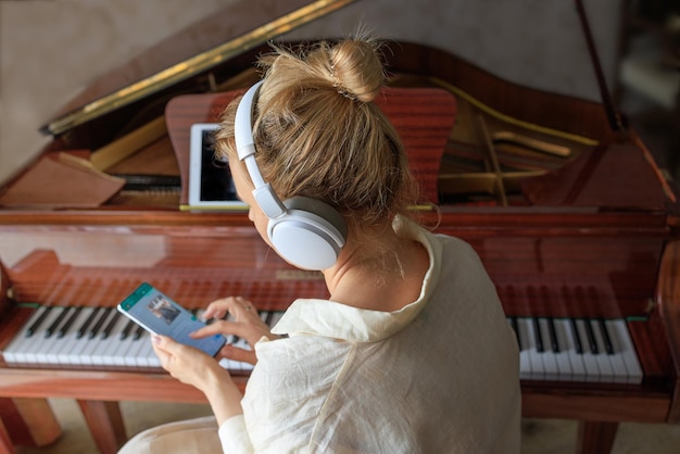 Young girl in headphones plays an antique piano and uses a smartphone to study