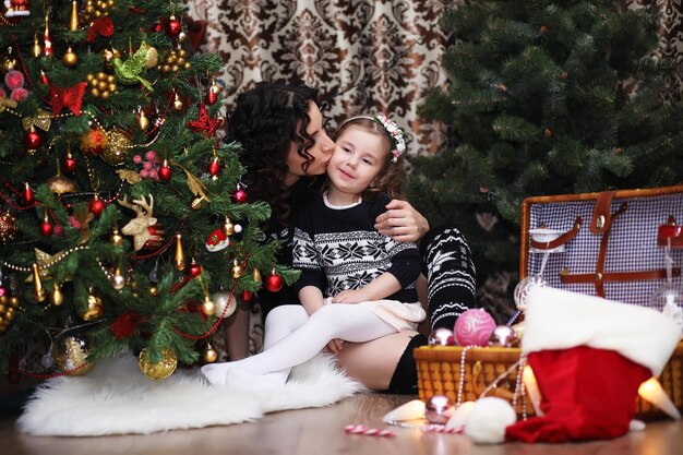 A young girl helps her mother to decorate the family Christmas tree Family winter holidays and people concept happy mother and little daughter at home