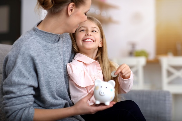 young girl and her mother with piggybank sitting at table