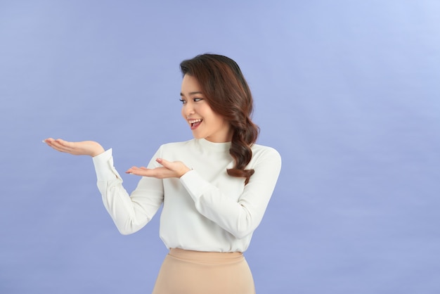 Young girl holding copyspace imaginary on the palm to insert an ad on purple background