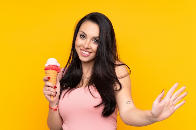 Young girl holding an cornet ice cream over yellow saluting with hand with happy expression