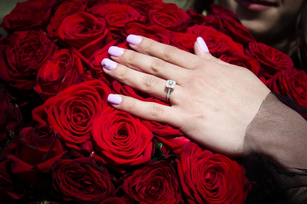 Young girl holding her hand with a wedding ring on a bouquet of roses