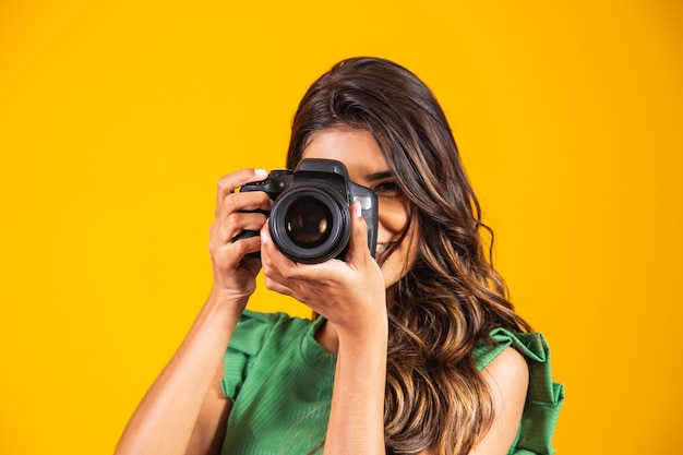 Young girl holding a photo camera on yellow background. woman taking picture