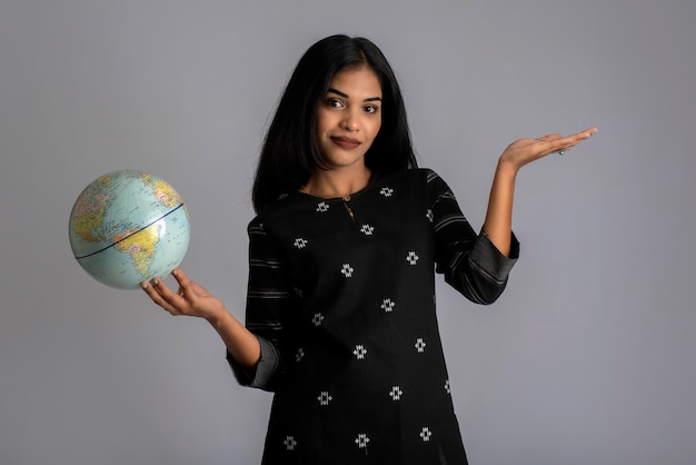 Young girl holding the world globe and posing on grey.