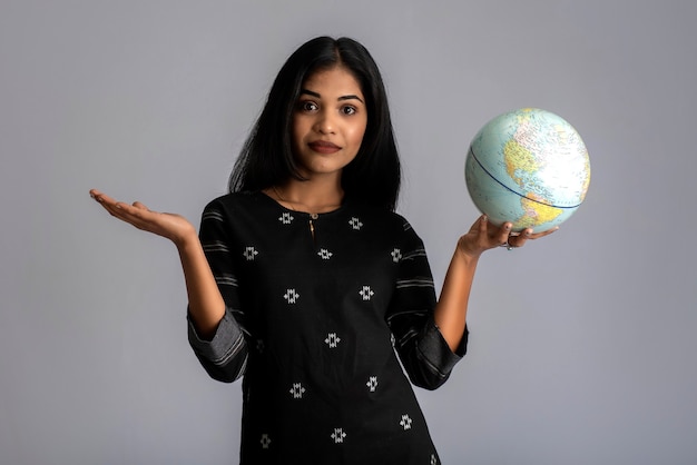 Young girl holding the world globe and posing on grey.