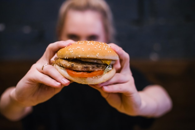 A young girl holds a burger with a meat patty in her hands.Delicious and hearty lunch. Fast food and snacks.