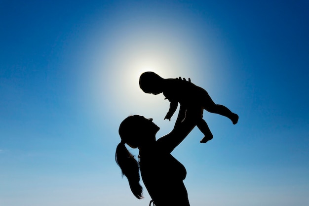 A young girl holds a child in her arms against the sun. Silhouette photography. High quality photo