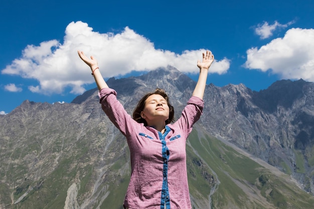 Young girl holds hands up against the sky and mountain