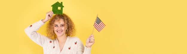 A young girl holds a model of a green house in her hands and an American flag The concept of buying an eco house