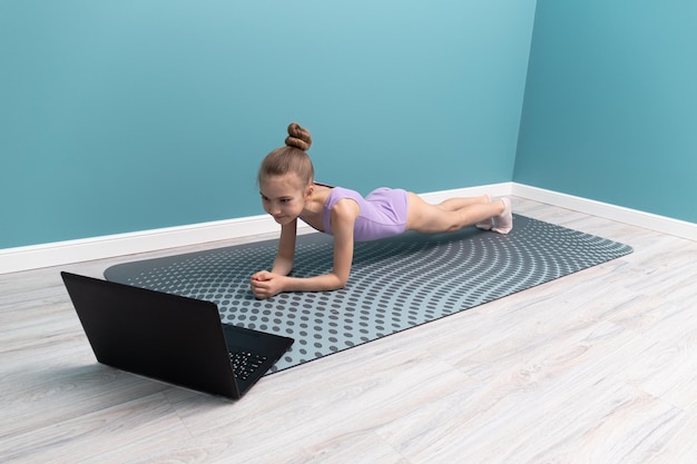 A young girl is doing gymnastics in front of a laptop Classes at home