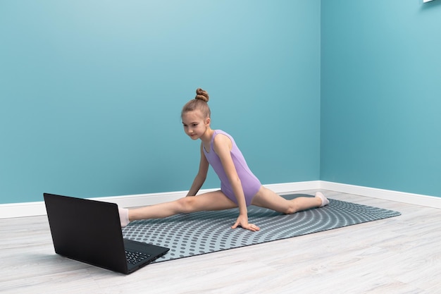 A young girl is doing gymnastics in front of a laptop Classes at home