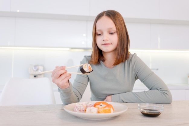 young girl is eating sushi with chopsticks