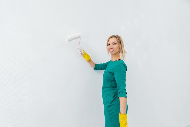 A young girl is engaged in repairs and paints a white wall with a roller in a new apartment Renovation of the interior and a new apartment Housewarming and a desirable mortgage