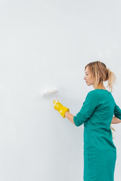 A young girl is engaged in repairs and paints a white wall with a roller in a new apartment Renovation of the interior and a new apartment Housewarming and a desirable mortgage