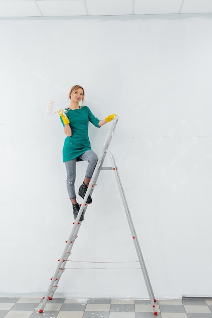 A young girl is engaged in repairs on the stairs and paints a white wall with a roller in a new apartment Renovation of the interior and a new apartment Housewarming and a desirable mortgage