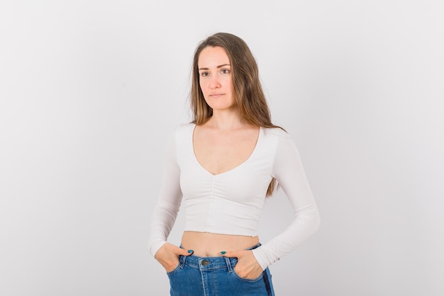 Young girl is keeping hands in pockets and looking away on white background