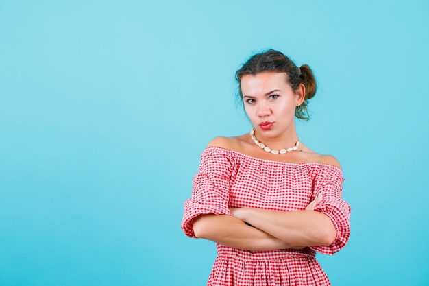 Young girl is looking away by crossing arms on blue background