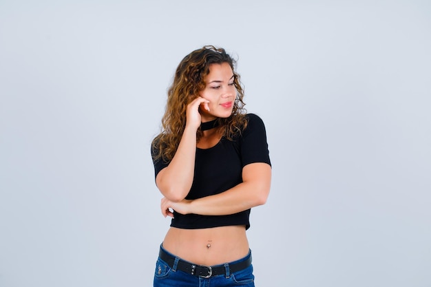 Young girl is looking down by holding hand on cheek on white background