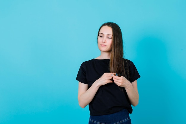 Young girl is looking down by holding her hair on blue background