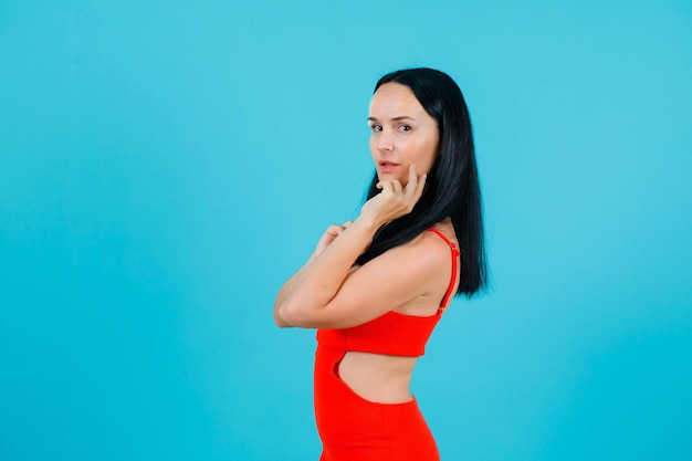 Young girl is posing to camera by holding hand on cheek on blue background