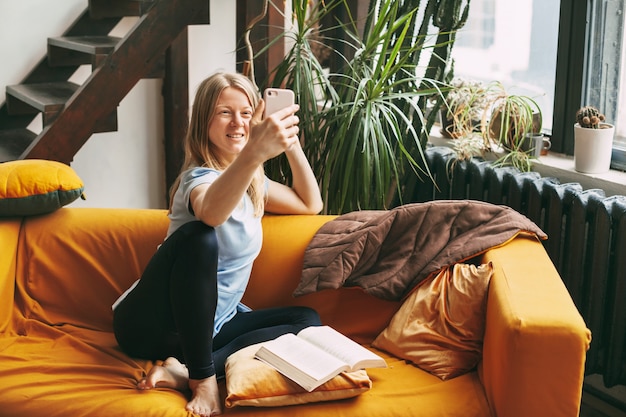 A young girl is sitting on the sofa and taking a selfie on her phone