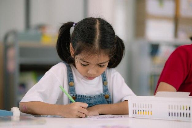 A young girl is sitting at a table with a green crayon in her hand