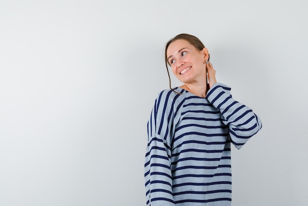 The young girl is smiling by holding her left hand to neck on white background.
.