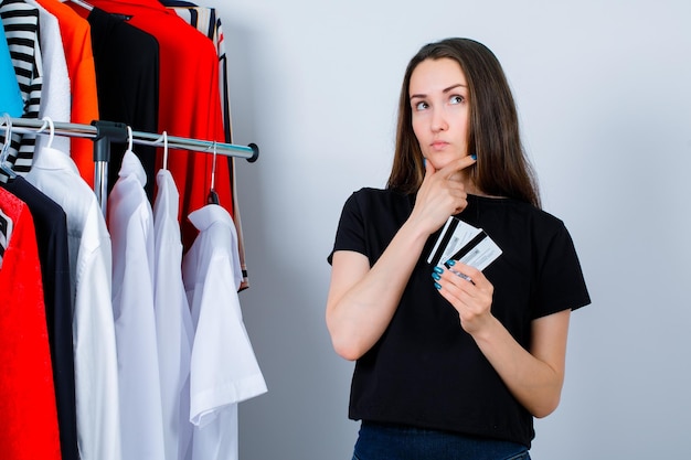 Young girl is thinking by holding credit cards on clothes background