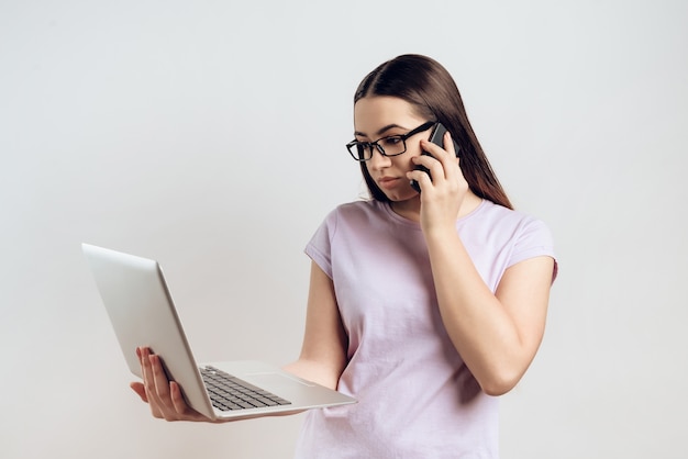 Young girl is typing on laptop while talking on phone.